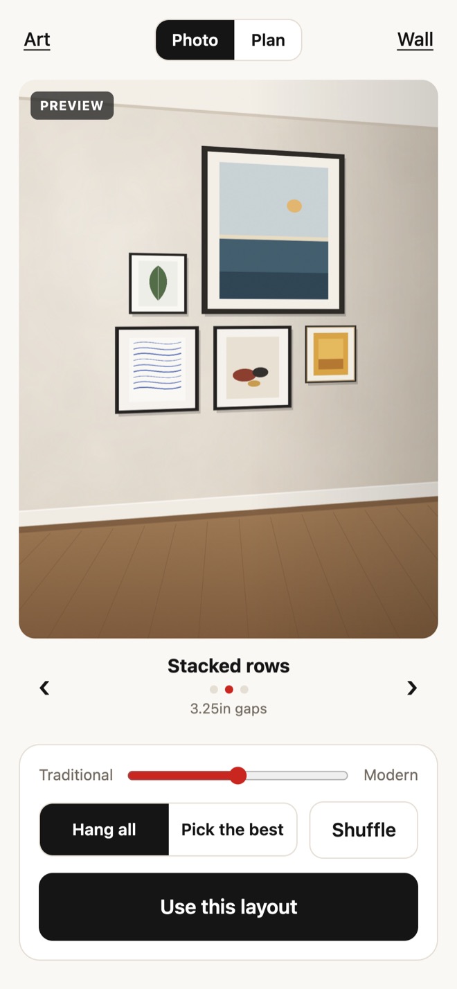 Hangsmith showing a layout called Stacked rows: five framed pieces drawn in perspective on a photo of a plaster wall, with the Traditional to Modern slider, Hang all, Pick the best, Shuffle, and Use this layout below.